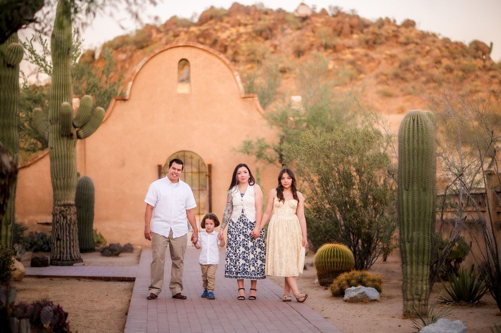 Family of four posing on a wooden path surrounded by saguaro cacti and a adobe building in the Arizona desert.