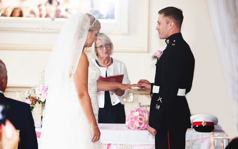 Military groom exchanges wedding rings with bride during elegant ceremony officiated by female minister. Surrey wedding photos