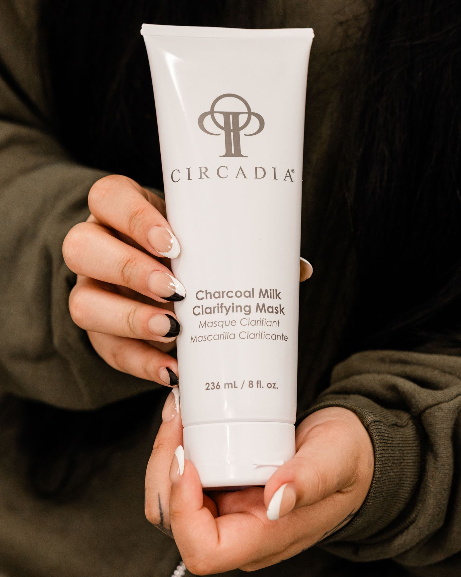 Hands holding Circadia Charcoal Milk Clarifying Mask tube, 8 fl oz skincare product.