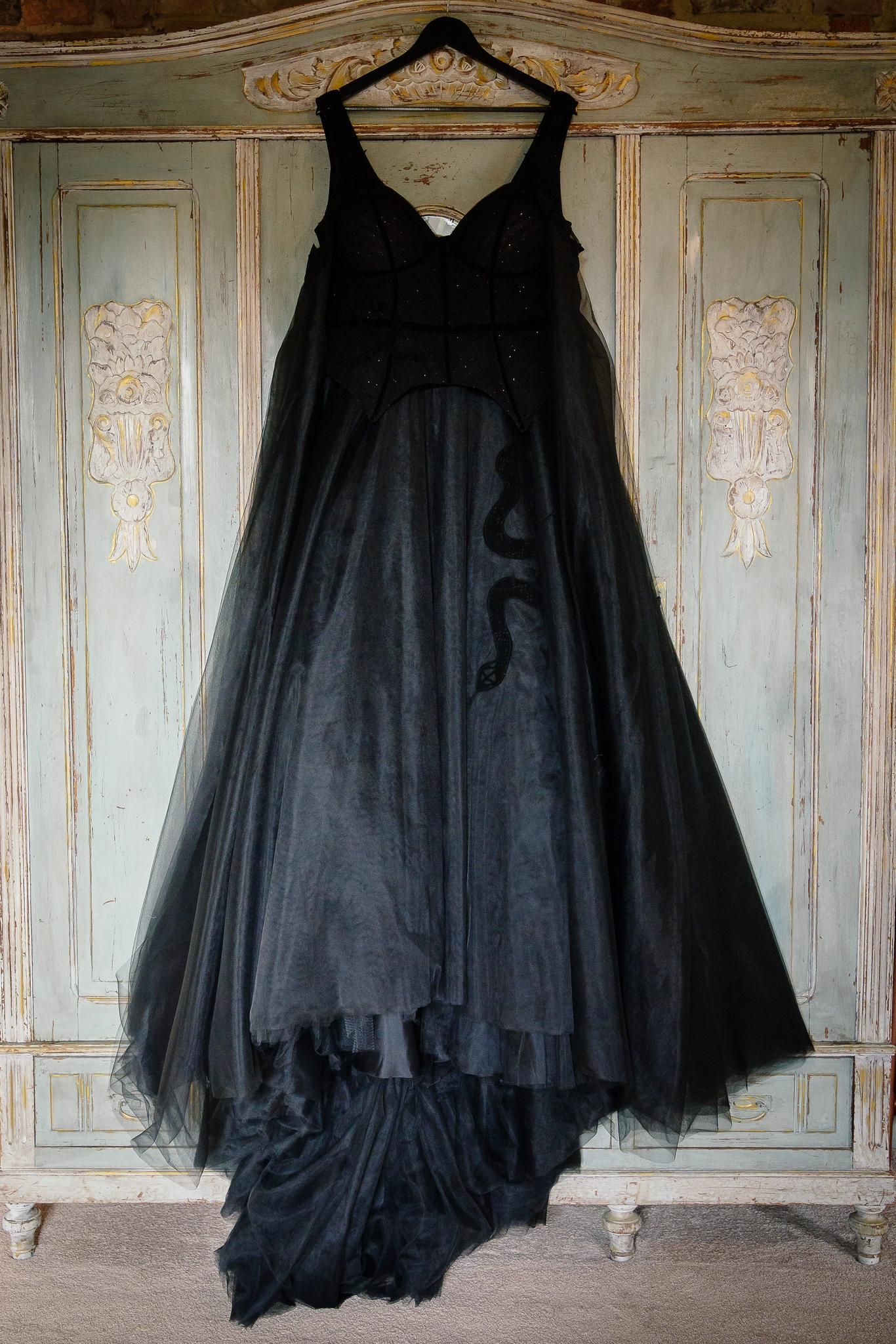 Black corset wedding dress with tulle skirt by Legend Bridal Design hanging on a painted wardrobe at Le Petit Chateau