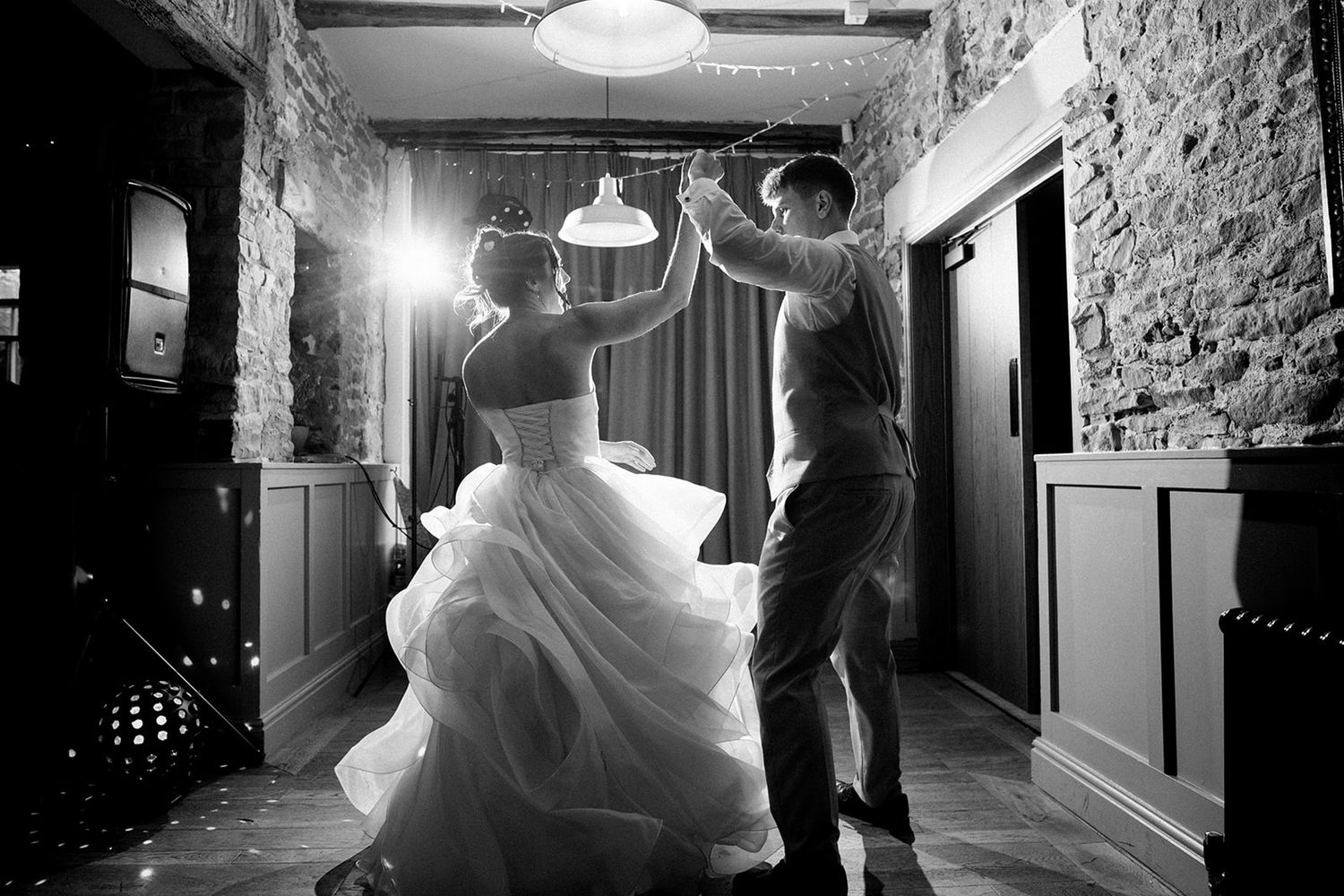 Black and white photo of a bride and groom holding hands and walking uphill through a grassy field with grazing sheep in the distance.