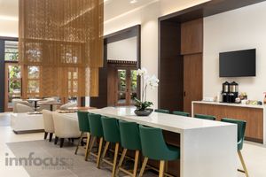 Modern hotel lounge with a long white communal table, green velvet chairs, white orchid centerpiece, wood accents and a coffee station.