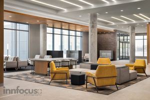 Modern hotel lobby lounge with mustard yellow armchairs, gray sofas, a long communal table, and floor-to-ceiling windows.