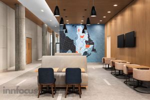 Modern hotel lobby with wood-paneled walls, pendant lights, a map mural, cushioned bench seating and navy chairs beside wall-mounted TVs.