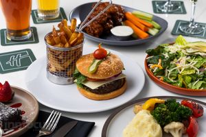 Table spread with a cheeseburger and fries in a wire basket, a fresh salad, ribs with dip, and a plate of mashed potatoes with broccoli.