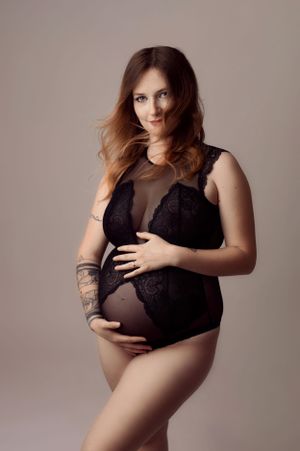 Pregnant woman in black lace lingerie cradling baby bump in professional maternity studio photo.