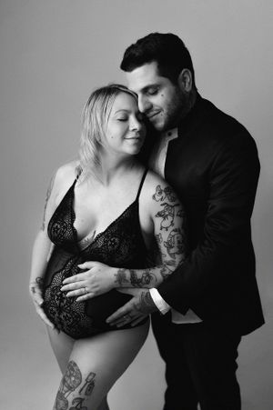 Black and white maternity photo of tattooed couple embracing tenderly in studio portrait.