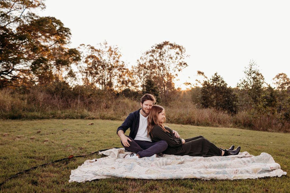 Couple relaxing on white blanket in field during golden hour sunset.