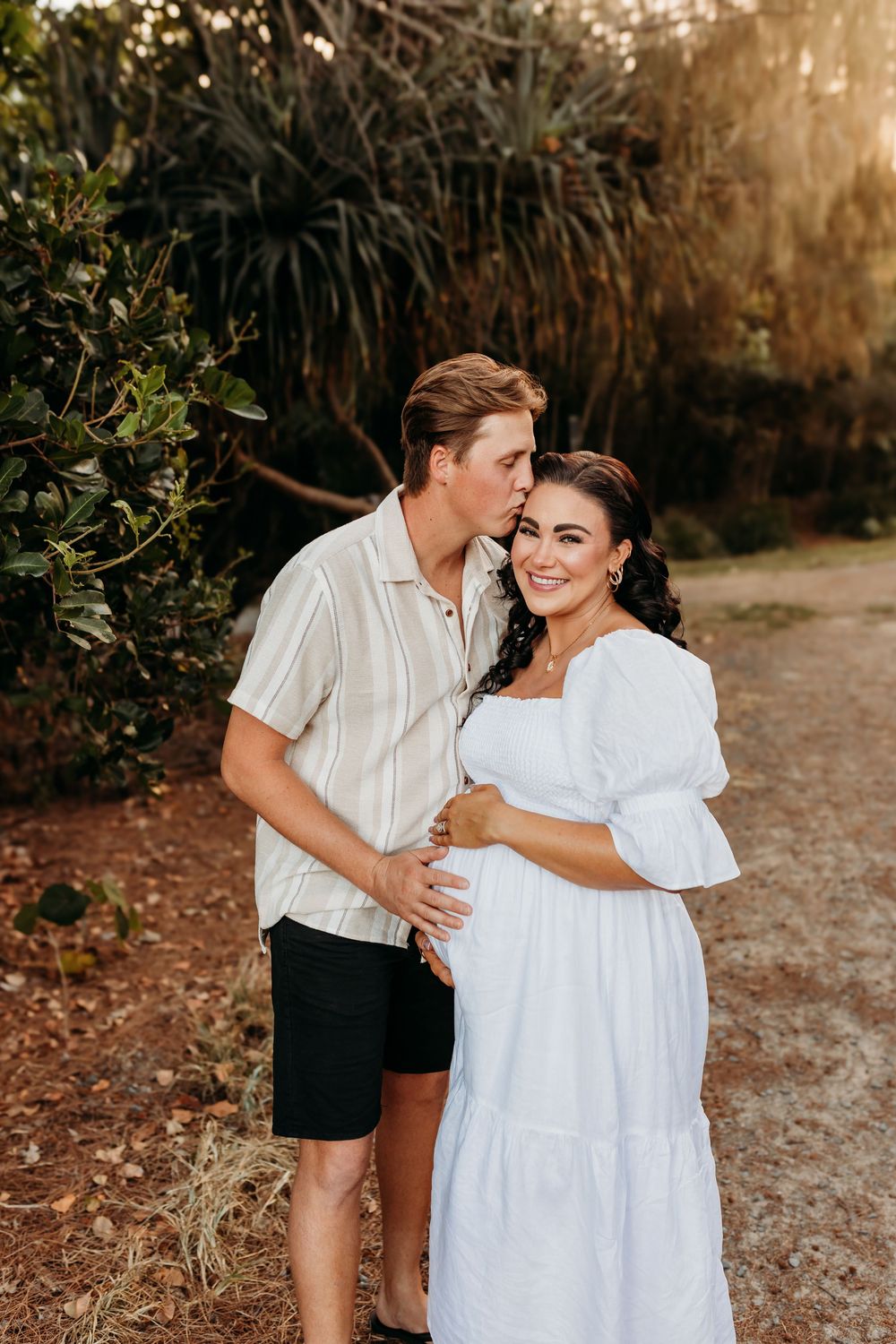 Romantic couple embracing in white outfits during golden hour outdoor photoshoot.