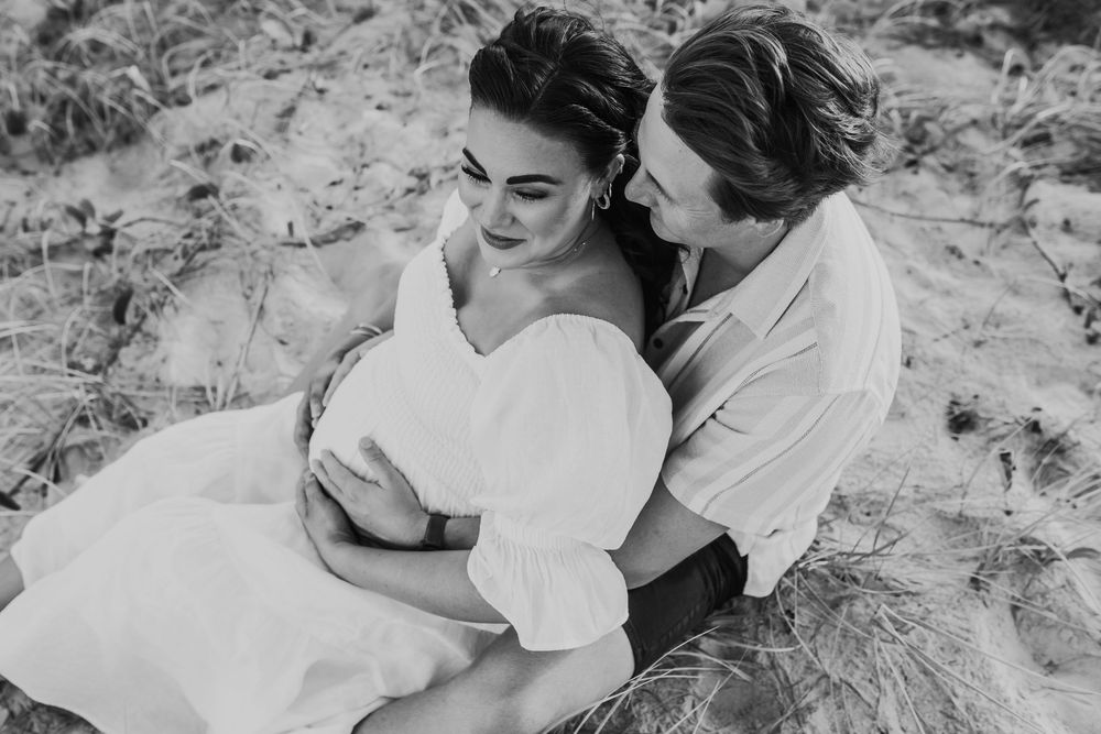 Intimate black and white beach photography session of couple lying in sand.