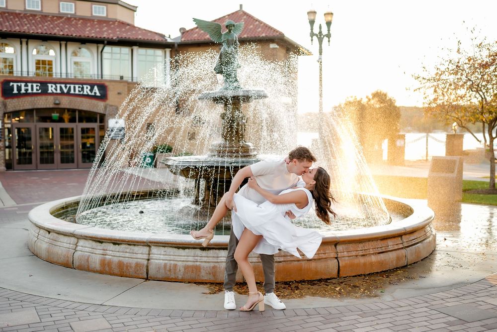 A couple in wedding attire poses romantically by a fountain during golden hour sunset.