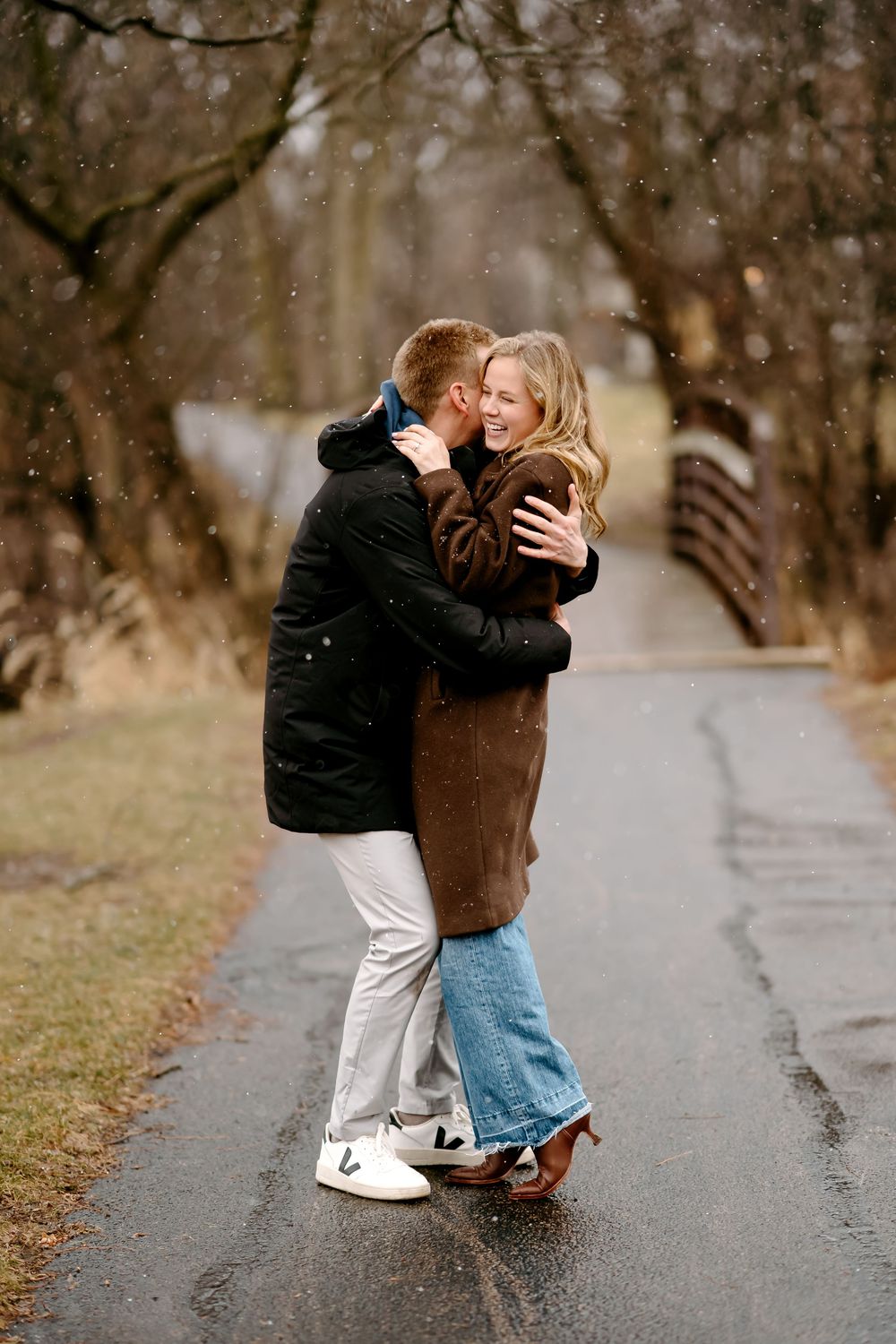 Two people share a romantic embrace on a misty path surrounded by bare winter trees.