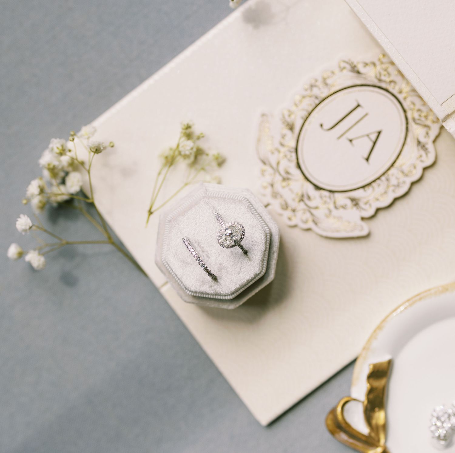 Diamond engagement ring in velvet ring box beside baby's breath flowers and monogram wedding stationery.