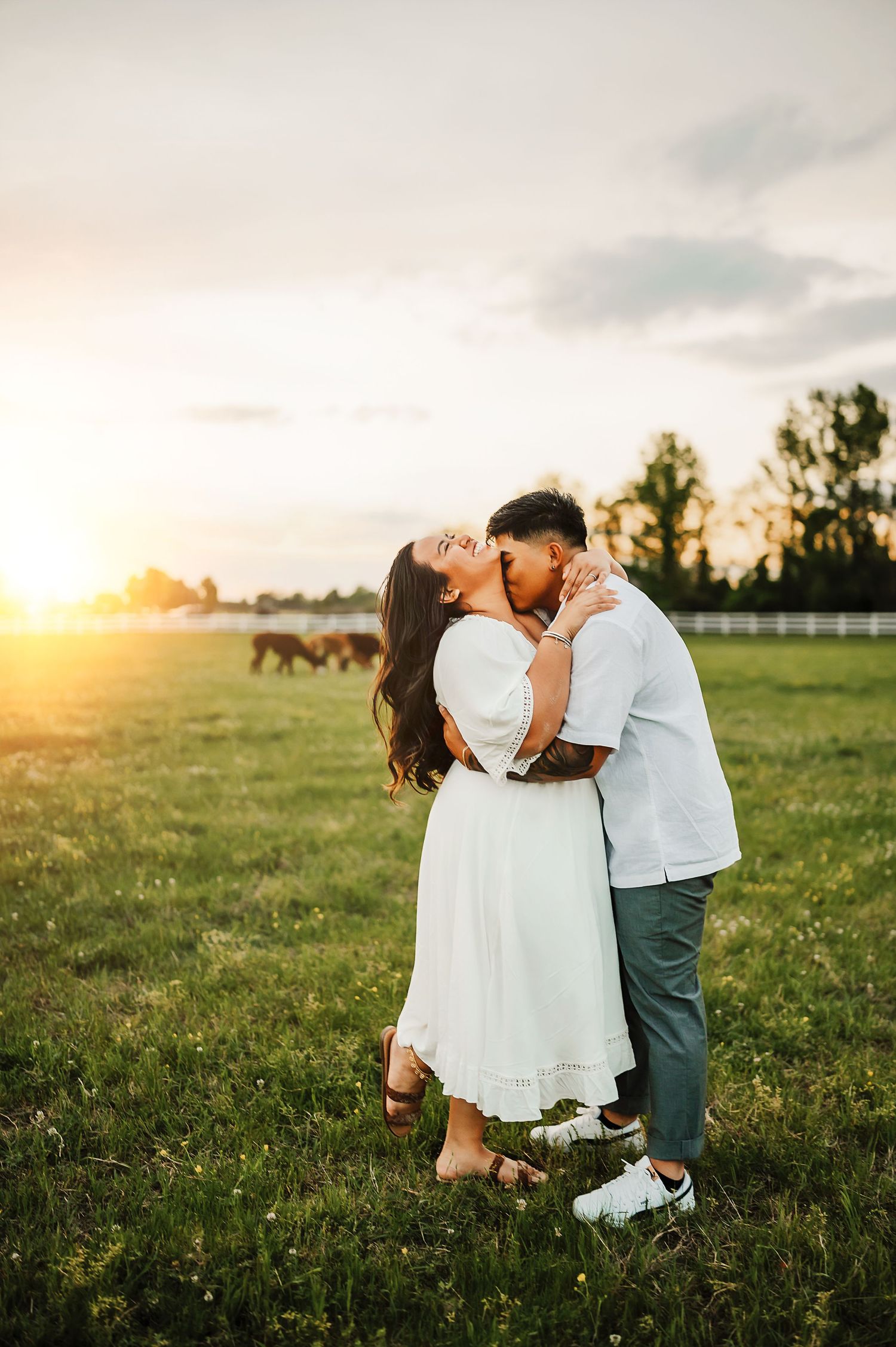 Romantic couple embracing in white outfits at sunset in pastoral field with horses. lake county couples photographer