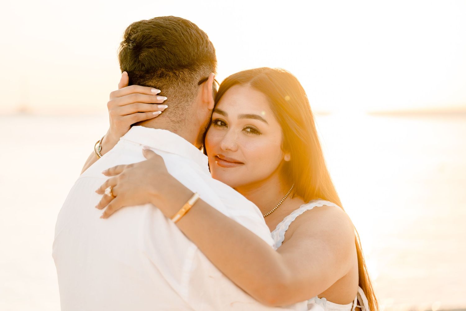 Couple embraces tenderly during golden hour on beach with sun flare in background. Grand Cayman