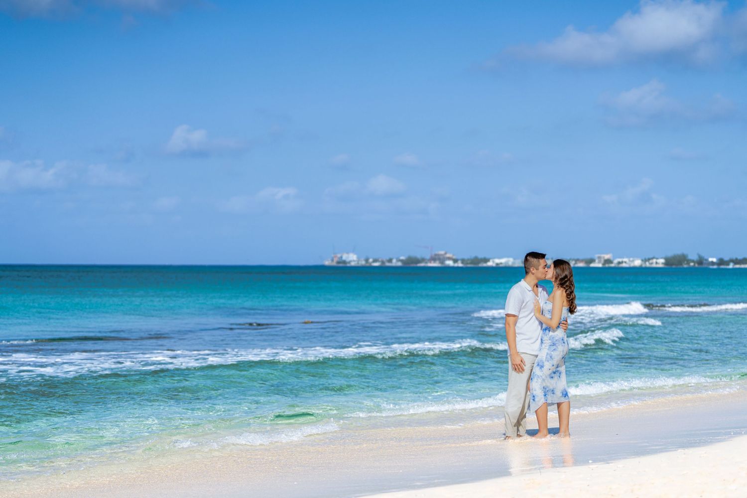 Two people embrace while walking along a pristine Caribbean beach with turquoise water and white sand.
