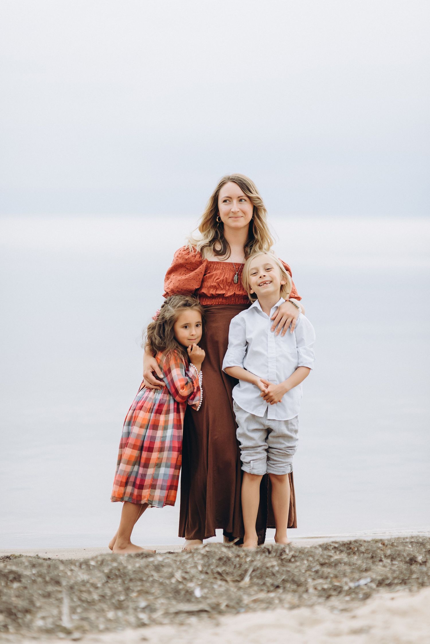 Young mom hugging her beautiful kids on the beach, happy family