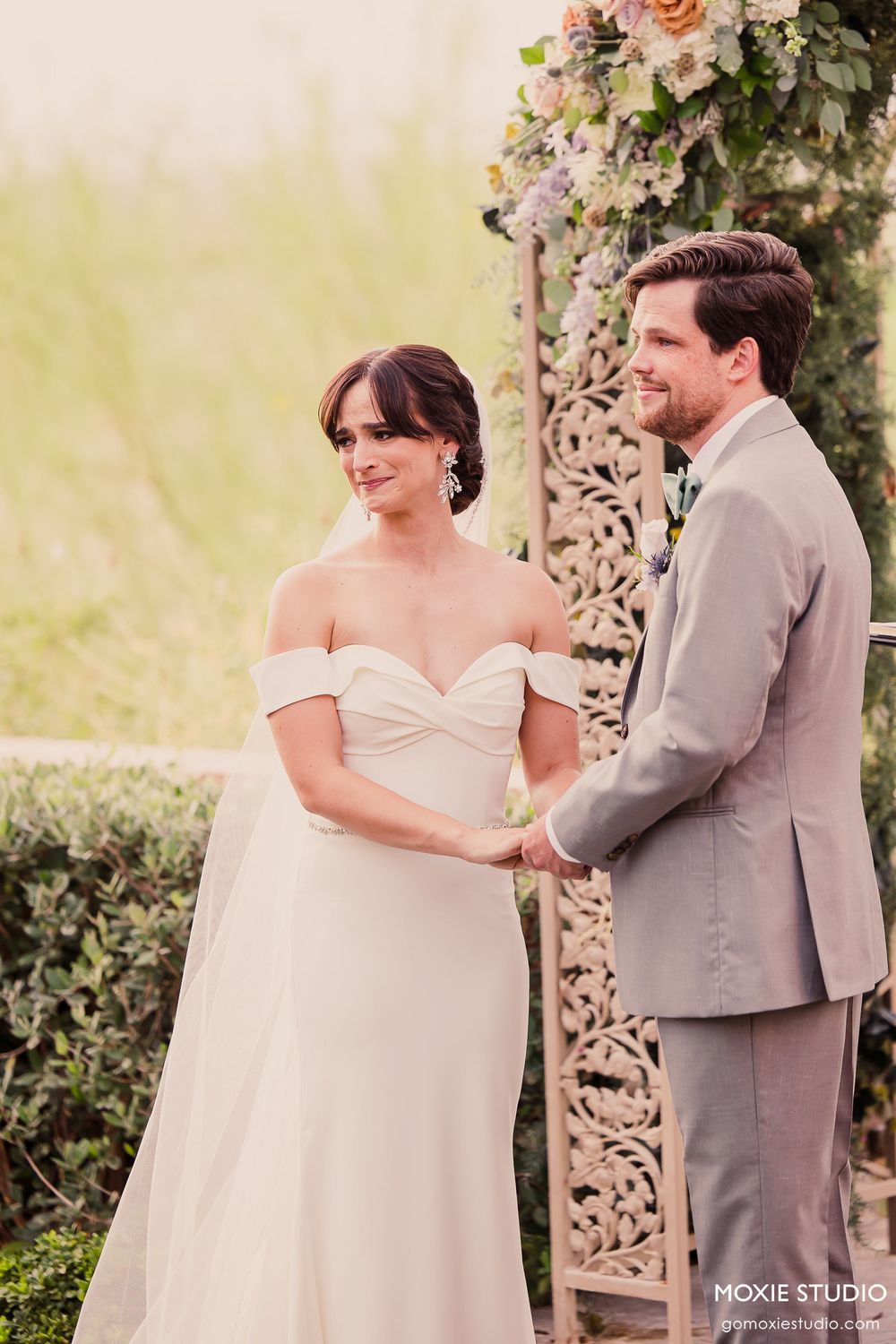 Couple shares intimate moment during wedding ceremony under decorative floral arch.