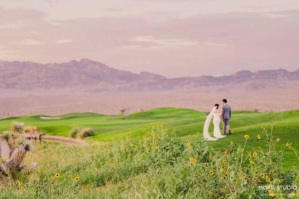 A couple walks on a lush green golf course with mountains in the background during sunset.