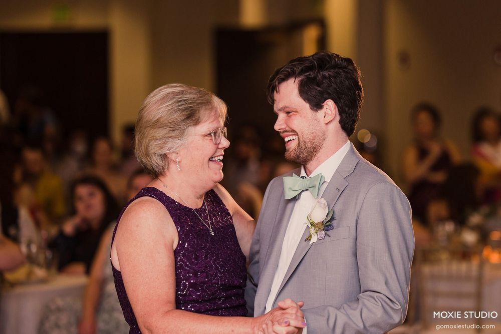 Two people share a heartfelt dance moment at a wedding reception with guests seated in the background.