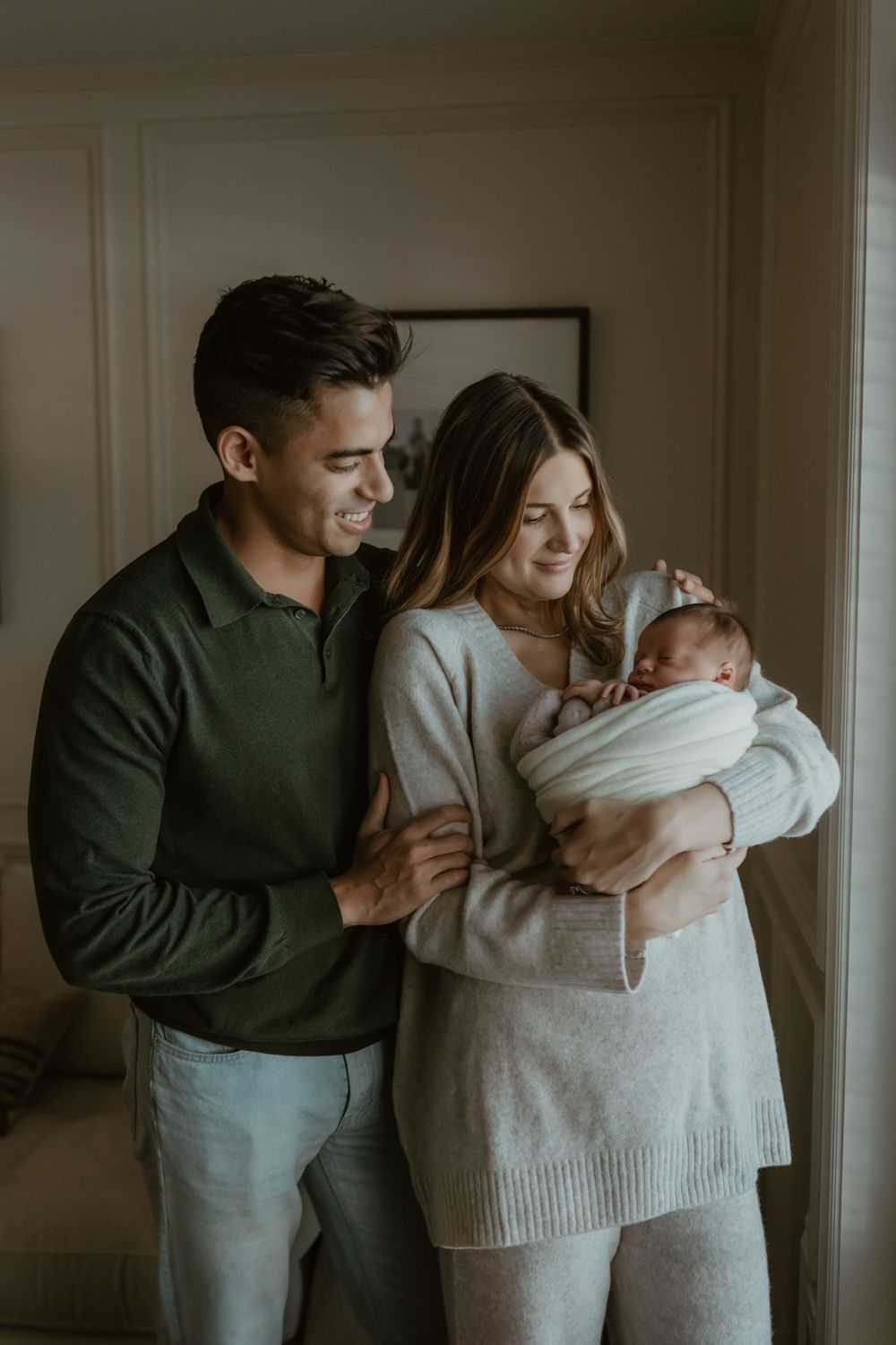 A family shares tender moments together in a cozy living room wearing neutral colored sweaters.