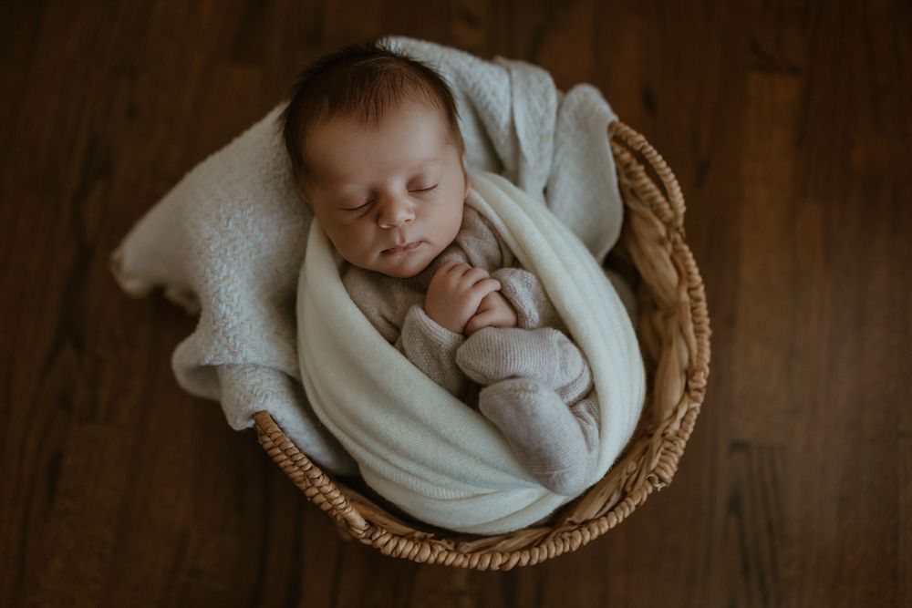 Peaceful sleeping newborn baby wrapped in white blanket nestled in woven basket with warm lighting.