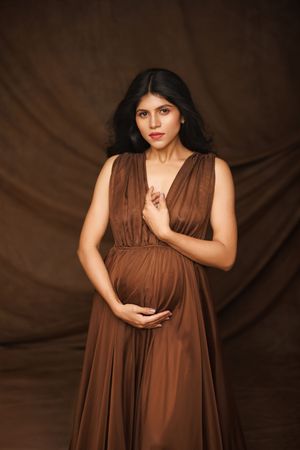 Fashion portrait featuring a flowing brown dress against a dark textured backdrop in dramatic lighting.