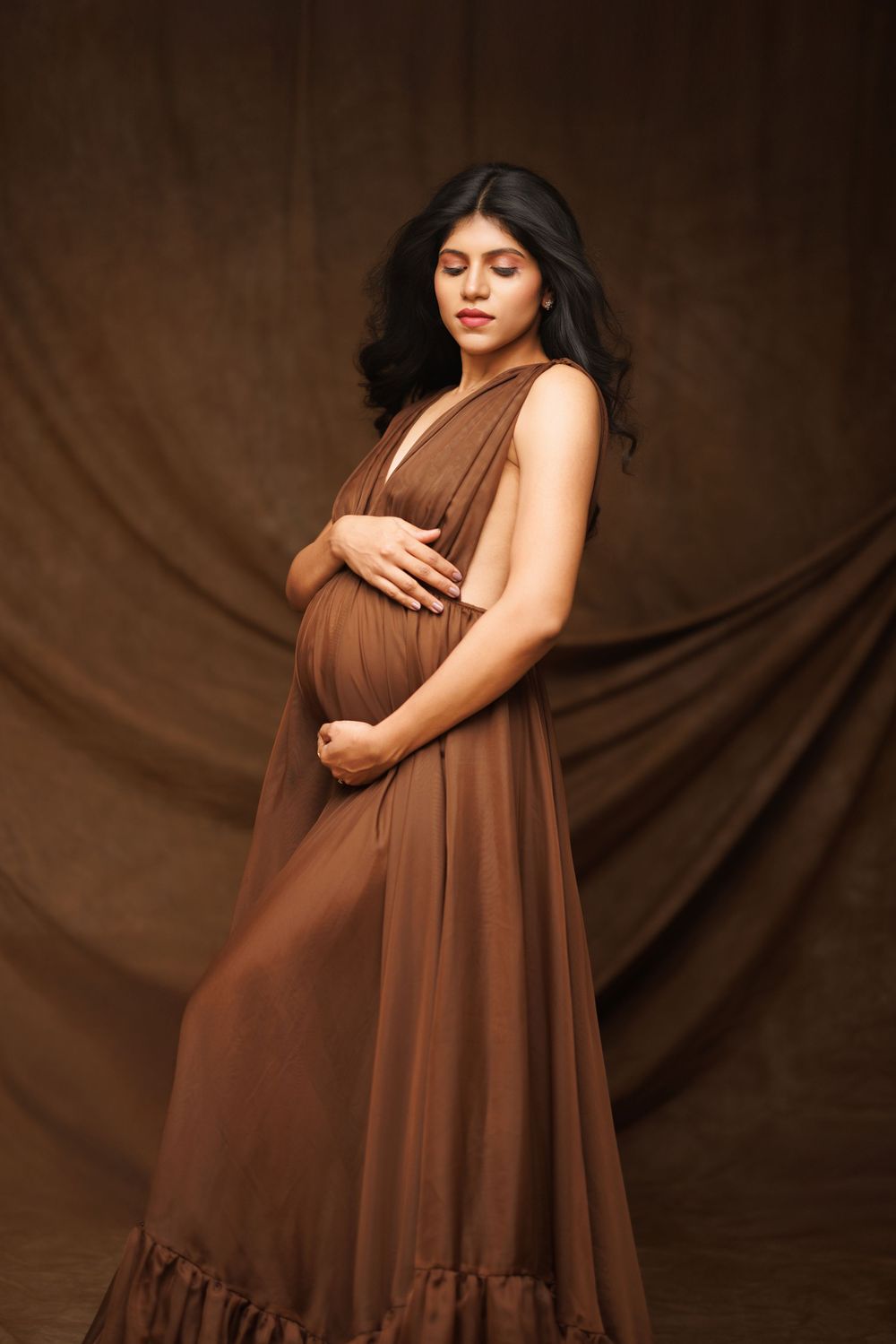 A series of artistic maternity photos showing a brown flowy dress against a dark backdrop.