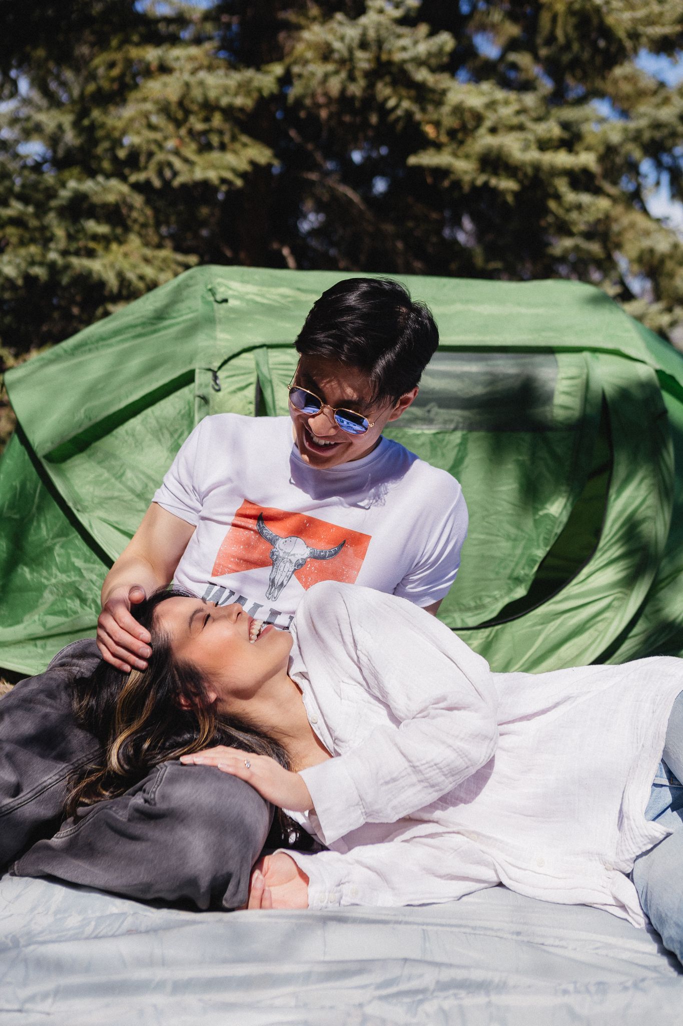 Couple relaxing on blanket outdoors with green tent in background.