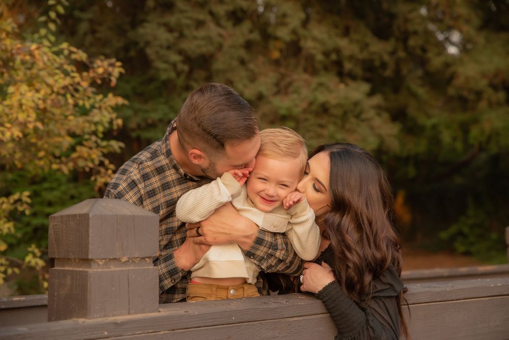 Parents kissing their smiling young child during an outdoor family portrait session.