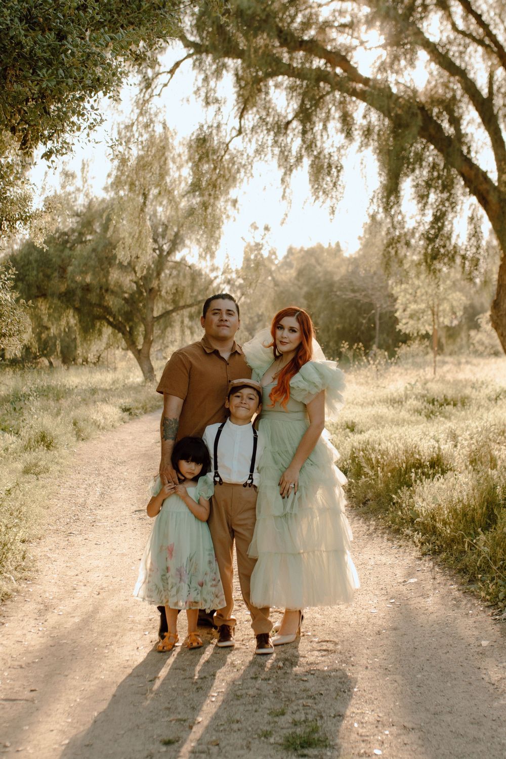 Family portrait on dirt path under dreamy willow tree at golden hour.