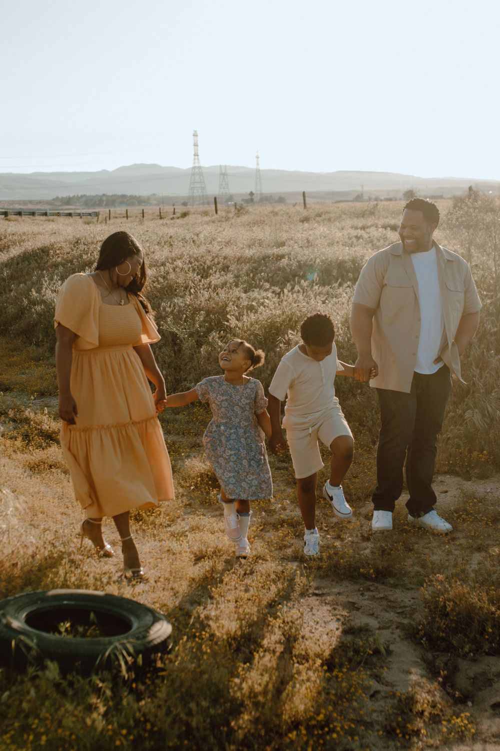 Family walking together at sunset in golden field with mountains in background.