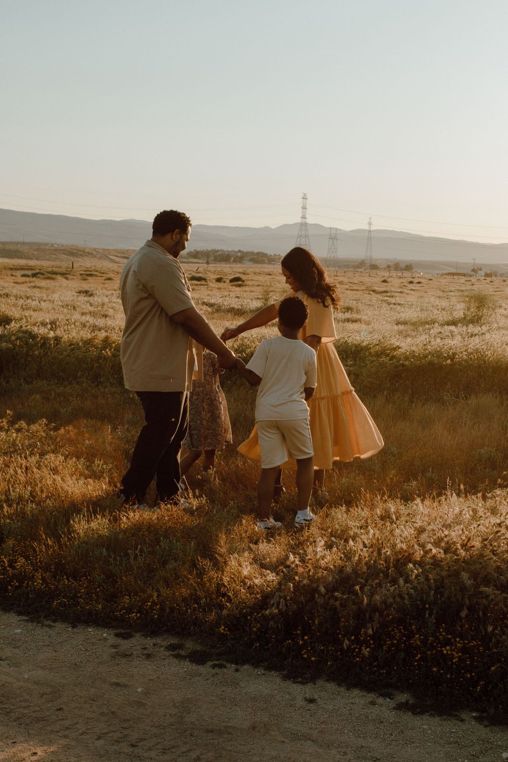 Family holding hands while enjoying sunset view in rural landscape.