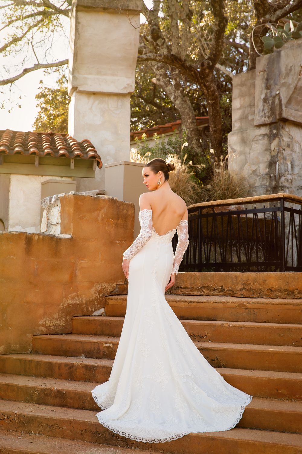 Elegant bride in lace white wedding dress twirls gracefully on stone steps during golden hour sunset.