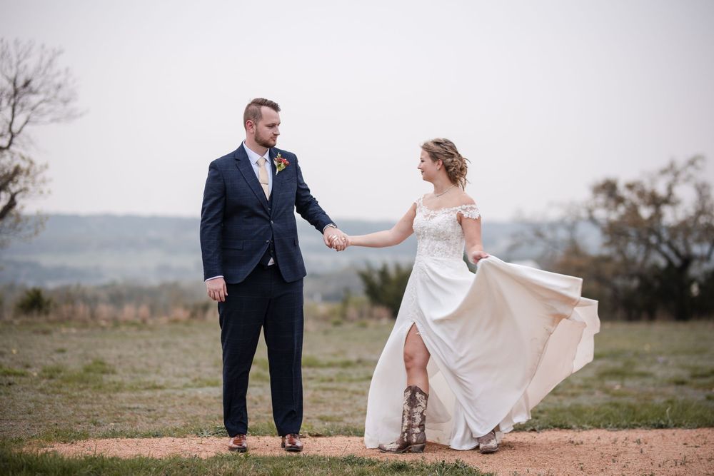 A couple in wedding attire poses together on a scenic hilltop during their outdoor photoshoot.