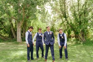 Four groomsmen in navy suits share a candid laughing moment on a lawn.