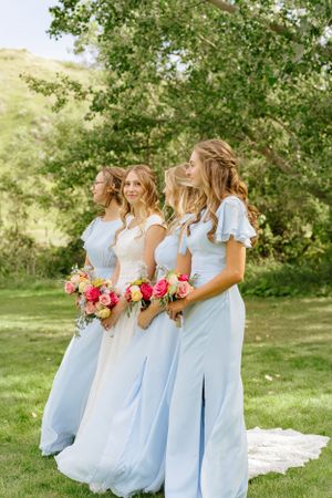 Wedding party in light blue dresses holding colorful bouquets pose in an outdoor garden setting.