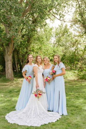 Bridal party in powder blue dresses pose with bride in lace gown outdoors.