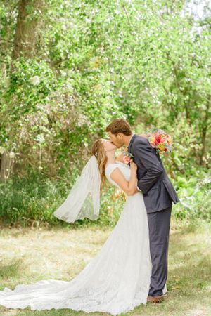 Romantic wedding couple embraces during outdoor photo session in wooded area.