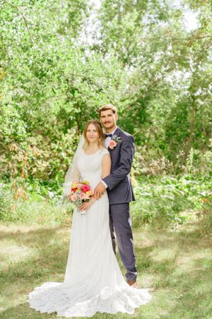 Newlywed couple poses together on grassy lawn surrounded by spring foliage.