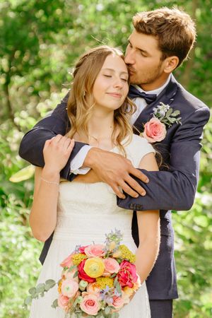Intimate moment between newlyweds with colorful bouquet in garden setting.