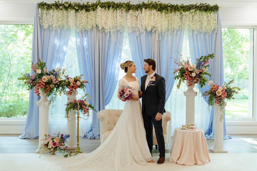 Wedding ceremony setup with light blue draping and floral arch featuring pink and white flowers.