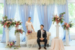 Elegant wedding setup with light blue draping and floral arrangements in an indoor venue.