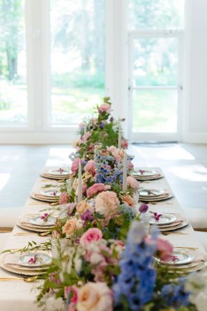 Elegant table setting with pink and blue floral centerpieces running down a white tablecloth.