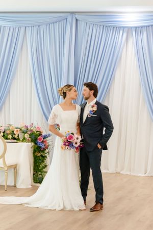 Wedding ceremony setup with light blue drapery backdrop and floral arrangements.