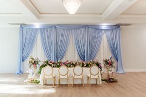 Wedding reception table with blue drape backdrop and elegant white chairs at the Norland Historic Estate Wedding & Event Venue.