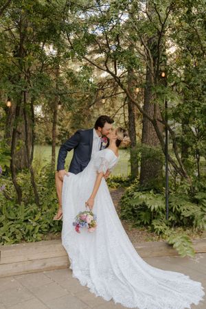 Wedding couple embracing on outdoor path surrounded by lush greenery with bride holding a pastel bouquet.