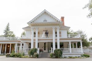 Classic white Southern mansion with prominent columns and wraparound porch during wedding celebration.