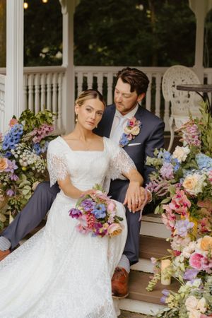 Romantic portrait in gazebo surrounded by lush floral arrangements in pink and purple hues.