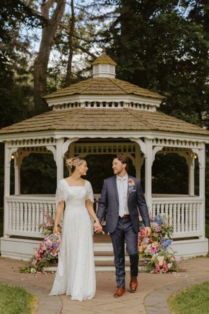White wooden gazebo decorated with pink and purple flowers for an outdoor wedding ceremony.
